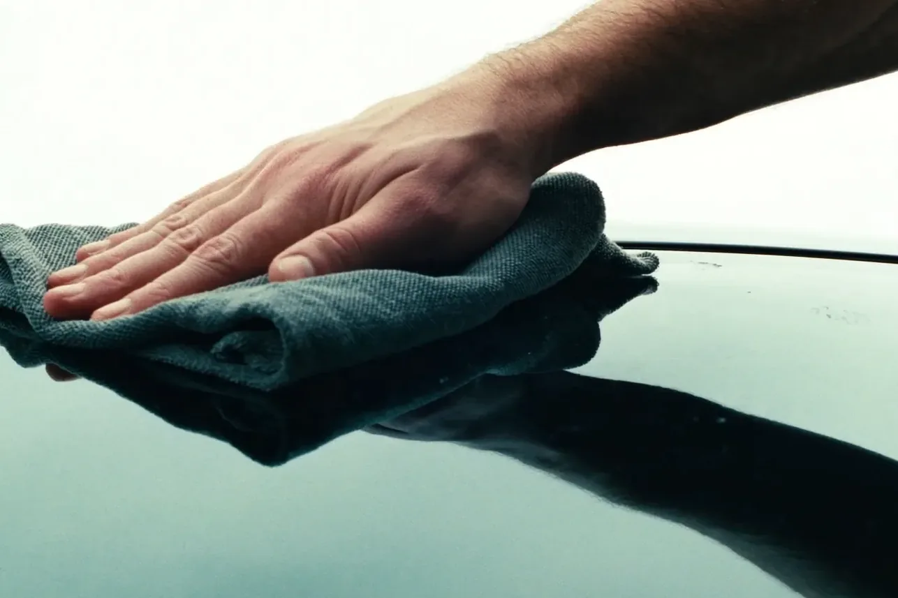 A hand wiping a newly installed windshield clean with a folded microfiber cloth.